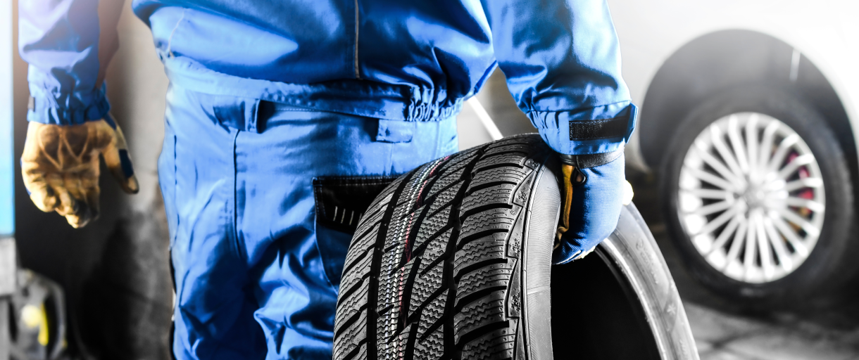 Closeup of mechanic in blue uniform carrying a tire over to a car