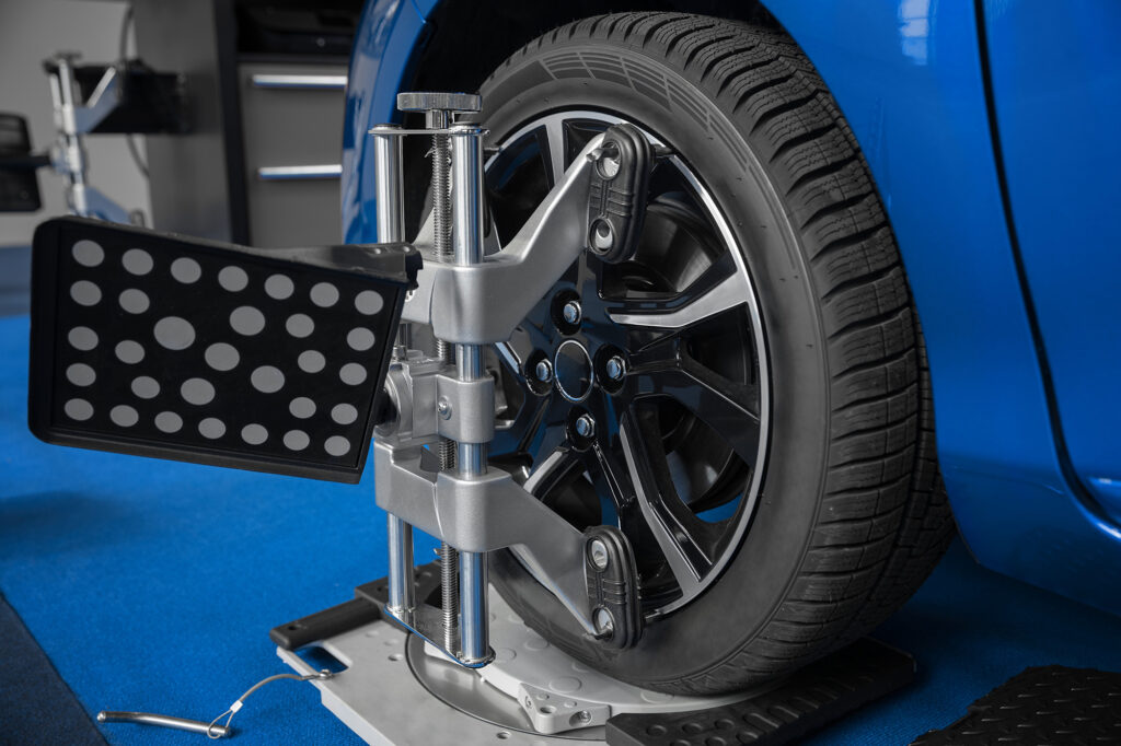 A car wheel is secured in a professional alignment machine, with calibration tools attached to the tire to measure its position and ensure proper alignment. The setup is part of a detailed process to adjust the vehicle’s suspension for optimal performance and tire longevity.