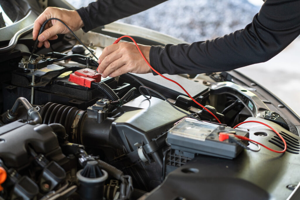 Close-up of hands conducting a battery voltage test with a multimeter.