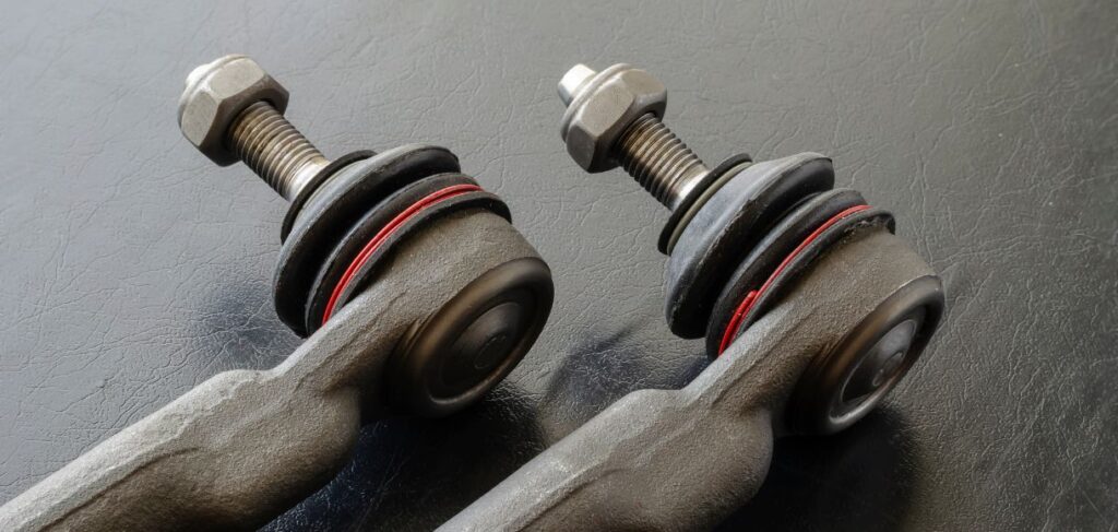 Close-up of two automotive tie rod ends with bolts and bushings, placed on a dark surface.