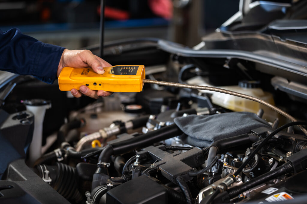 A mechanic uses a handheld yellow diagnostic tool with a flexible probe to inspect the engine of a vehicle, ensuring accurate maintenance and troubleshooting.