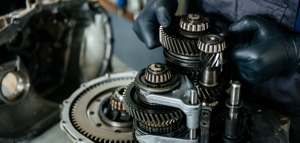 Mechanic wearing black gloves working on a car transmission, adjusting gears and components during a rebuild or repair.