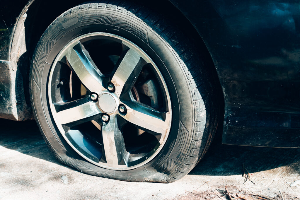 A person inflating a car tire and checking its pressure using an air pressure gauge with a connected hose.